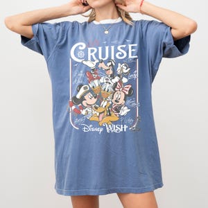 May include: Blue t-shirt featuring a graphic of Disney characters including Mickey Mouse, Minnie Mouse, Donald Duck, and Goofy. The shirt has the words "Cruise" and "Disney Wish" printed on it.