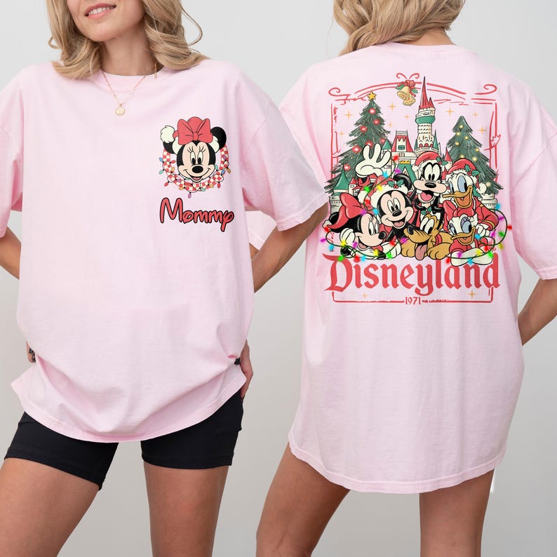 K&ouml;nnte beinhalten: Hellrosa T-Shirt mit Minnie Mouse und dem Wort "Mommy" auf der Vorderseite. Auf der R&uuml;ckseite des T-Shirts befindet sich ein Disneyland-Design mit Mickey, Donald und Goofy sowie Lichterketten und Weihnachtsb&auml;umen.