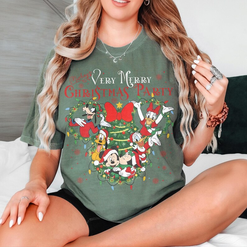 May include: Green t-shirt featuring a festive design with Mickey Mouse, Minnie Mouse, Donald Duck, Daisy Duck, Goofy, and Pluto. The shirt has the text "Very Merry Christmas Party" in red and white, with a Christmas tree and lights.
