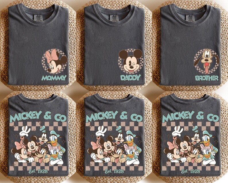 K&ouml;nnte beinhalten: Sechs anthrazitfarbene T-Shirts mit Disney-Charaktergrafiken. Drei Shirts haben individuelle Charakterdesigns mit den Worten "Mommy", "Daddy" und "Brother". Die anderen drei Shirts zeigen eine Gruppengrafik mit "Mickey & Co Est. 1928".