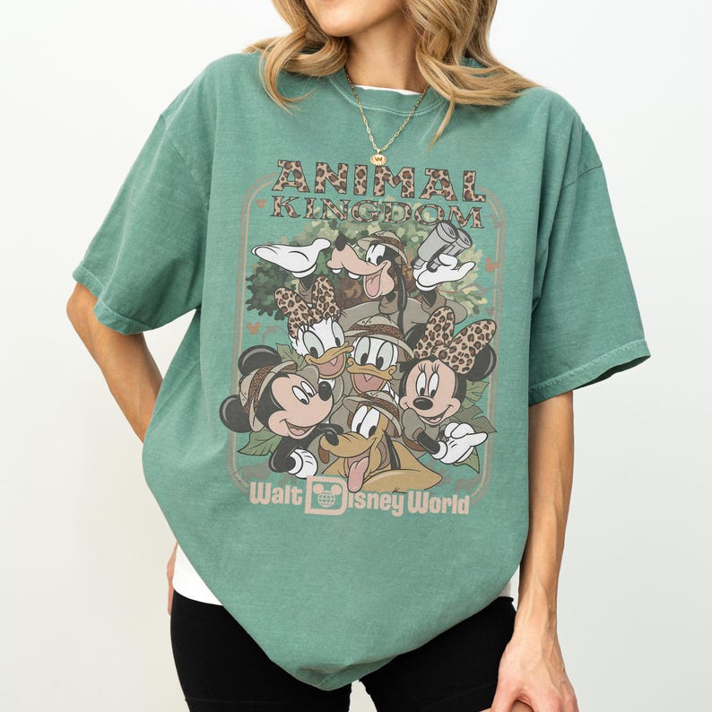 May include: Green t-shirt featuring a graphic of Disney characters, including Mickey and Minnie Mouse, Donald and Daisy Duck, and Goofy. The text "Animal Kingdom" and "Walt Disney World" are also displayed on the shirt.