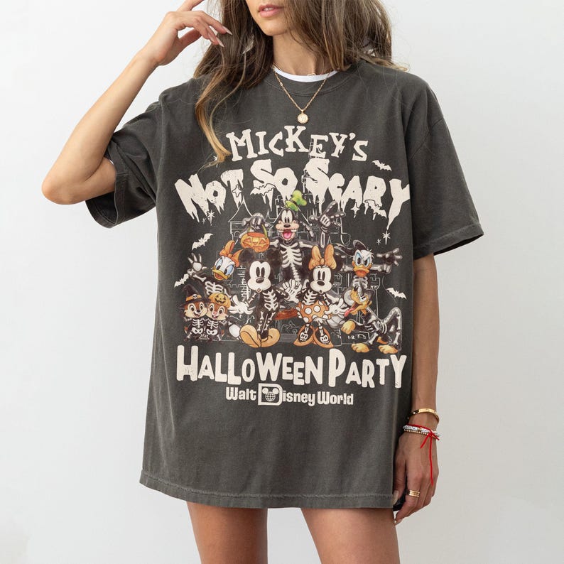 May include: Dark gray t-shirt featuring a Halloween-themed graphic. The design includes Mickey Mouse, Minnie Mouse, Donald Duck, and other Disney characters in skeleton costumes. Text on the shirt reads "Mickey's Not So Scary Halloween Party" and "Walt Disney World."