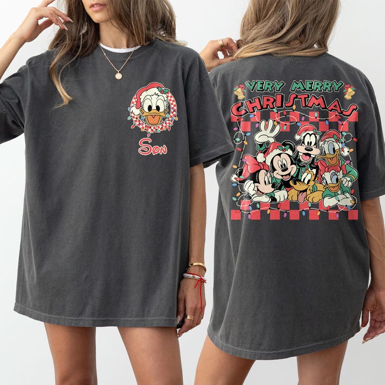 May include: Dark grey t-shirt with a Christmas design. The front shows Donald Duck in a Santa hat and the word "Son". The back has a "Very Merry Christmas" graphic with Mickey, Minnie, Goofy, Donald, and Daisy Duck.