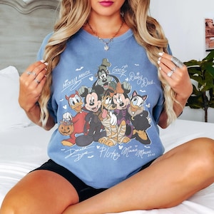 Puede incluir: Una camiseta azul de cuello redondo con un estampado gr&aacute;fico de personajes de Disney con disfraces de Halloween, incluyendo a Mickey Mouse, Minnie Mouse, Donald Duck, Goofy, Pluto y Daisy Duck, con sus nombres escritos en blanco alrededor.