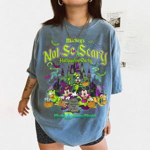 May include: A blue t-shirt featuring a graphic print of Mickey's Not-So-Scary Halloween Party with Disney characters in costumes, a castle, bats, and pumpkins. The text reads Mickey's Not-So-Scary Halloween Party, Trick or Treat, and Walt Disney World.