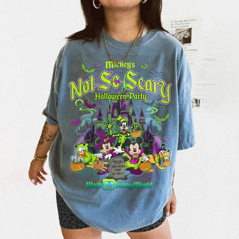 May include: A blue t-shirt featuring a graphic print of Mickey's Not-So-Scary Halloween Party with Disney characters in costumes, a castle, bats, and pumpkins. The text reads Mickey's Not-So-Scary Halloween Party, Trick or Treat, and Walt Disney World.