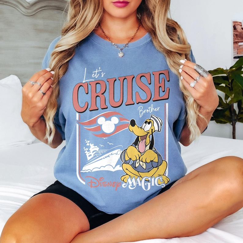 May include: A light blue t-shirt with the text "Let's Cruise Brother" and a graphic of Pluto in a sailor outfit. The design includes a cruise ship, a Mickey Mouse head, and the words "Disney Magic".