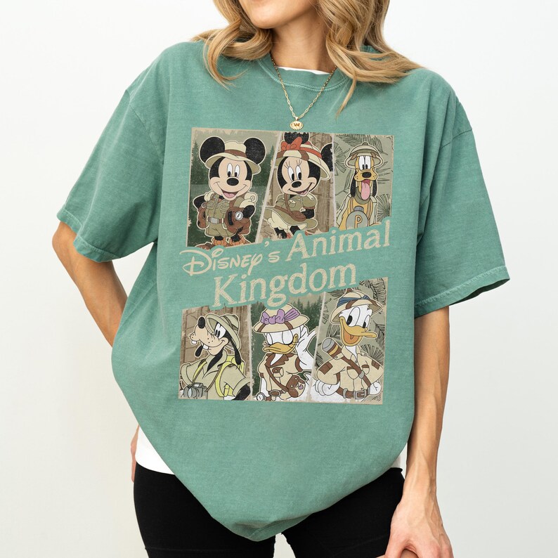 May include: A green t-shirt featuring a graphic of Disney's Animal Kingdom characters, including Mickey Mouse, Minnie Mouse, Pluto, Goofy, Donald Duck, and Daisy Duck. The shirt has a crew neck and short sleeves. The text "Disney's Animal Kingdom" is printed on the shirt.