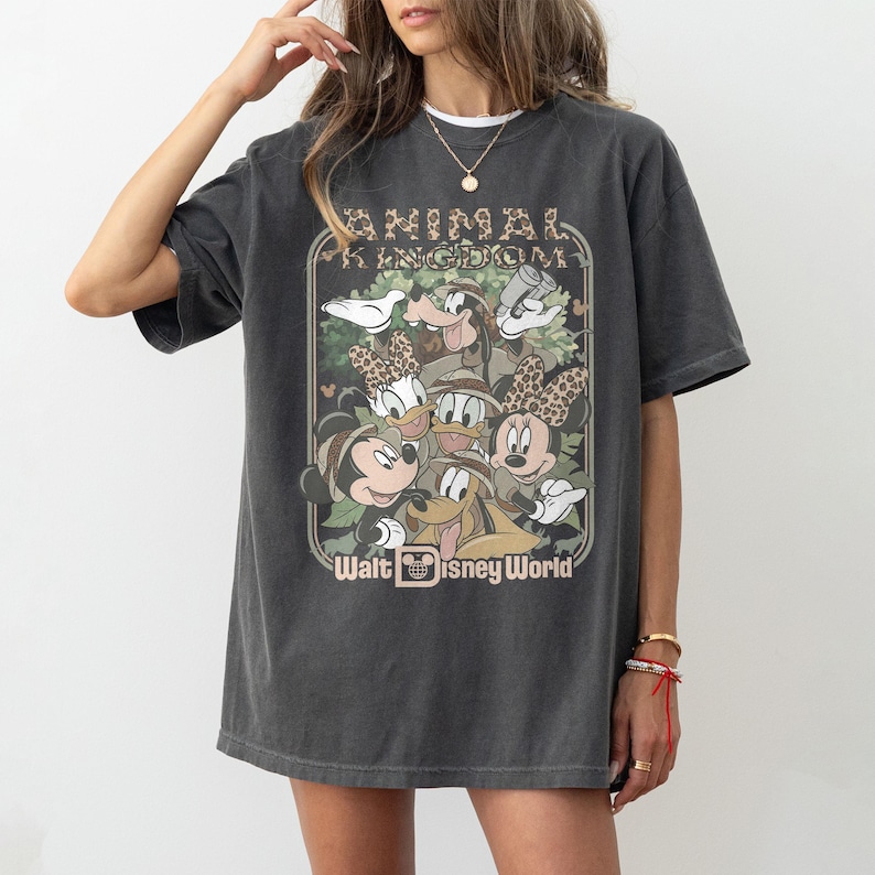 May include: Dark gray t-shirt featuring a vintage-style graphic of Disney characters, including Mickey and Minnie Mouse, Donald and Daisy Duck, and Goofy. The text "ANIMAL KINGDOM" and "Walt Disney World" are also displayed on the shirt.