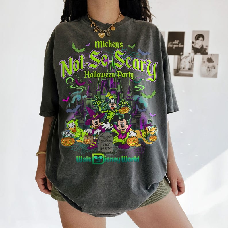 May include: A charcoal gray t-shirt featuring a graphic print of Mickey Mouse and friends in Halloween costumes. The text reads Mickey's Not-So-Scary Halloween Party and Walt Disney World. The design includes a castle, bats, and pumpkins.