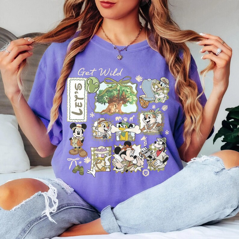 May include: A purple t-shirt with the text "Get Wild" and "Let's" printed on it. The shirt features cartoon characters in safari outfits, including Mickey Mouse, Donald Duck, and Chip and Dale. The design includes a tree and other safari-themed elements.