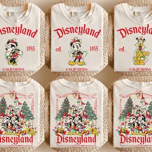 May include: Cream-colored t-shirts with the Disneyland logo in red, featuring Mickey Mouse, Pluto, and a group of Disney characters. The shirts have the text "est. 1955 CALIFORNIA" and "1971" printed on them.