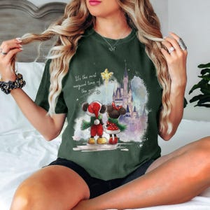 Pu&ograve; includere: T-shirt verde scuro con un'illustrazione festiva di Topolino e Minnie Mouse in abiti natalizi, davanti a un castello. La maglietta include il testo "It's the most magical time of the year."