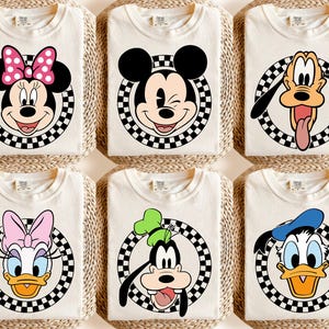 May include: Six cream-coloured t-shirts featuring Disney characters: Minnie Mouse, Mickey Mouse, Pluto, Daisy Duck, Goofy, and Donald Duck. Each character is centered on a black and white chequered circle.