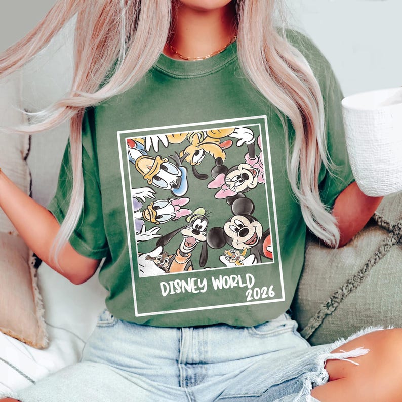 Puede incluir: Camiseta verde con un gr&aacute;fico enmarcado de personajes de Disney, incluyendo Mickey Mouse, Donald Duck y Goofy. El gr&aacute;fico est&aacute; sobre un fondo verde e incluye el texto "DISNEY WORLD 2026".
