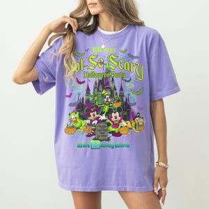 May include: A light purple t-shirt featuring a graphic print of Disney characters in Halloween costumes, including Mickey Mouse, Minnie Mouse, Donald Duck, Goofy, and Pluto. The text reads Mickey's Not-So-Scary Halloween Party and Walt Disney World.