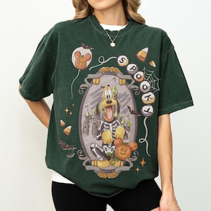 May include: Dark green t-shirt featuring a Halloween-themed graphic. The graphic includes Pluto in a skeleton costume, a pumpkin, a castle, and the word "Spooky". Additional elements include bats, candy corn, and a Mickey Mouse balloon.