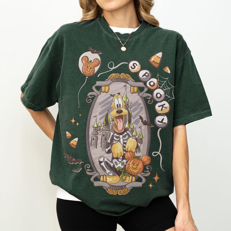 May include: Dark green t-shirt featuring a Halloween-themed graphic. The graphic includes Pluto in a skeleton costume, a pumpkin, a castle, and the word "Spooky". Additional elements include bats, candy corn, and a Mickey Mouse balloon.
