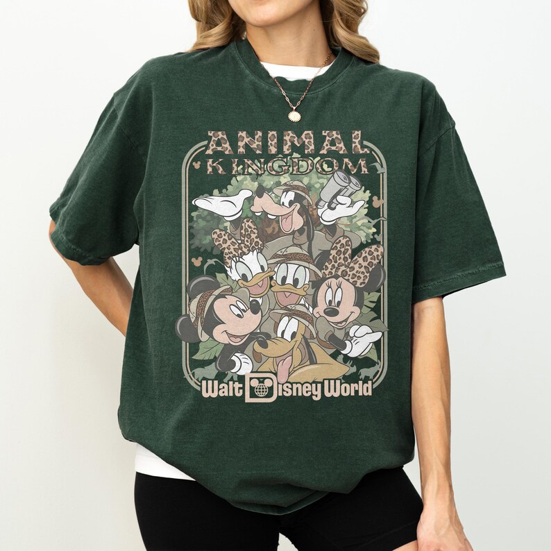 May include: Dark green t-shirt featuring a graphic of Disney characters, including Mickey and Minnie Mouse, Donald and Daisy Duck, and Goofy. The graphic is framed by the words "ANIMAL KINGDOM" and "Walt Disney World". The shirt has a vintage, worn look.
