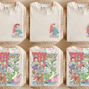 K&ouml;nnte beinhalten: Sechs cremefarbene T-Shirts. Drei Shirts haben Charaktergrafiken mit den W&ouml;rtern "Mommy", "Daddy" und "Brother". Die anderen drei Shirts haben eine "Toy Story"-Grafik mit Charakteren, dem Text "Since 1995" und Charakternamen.