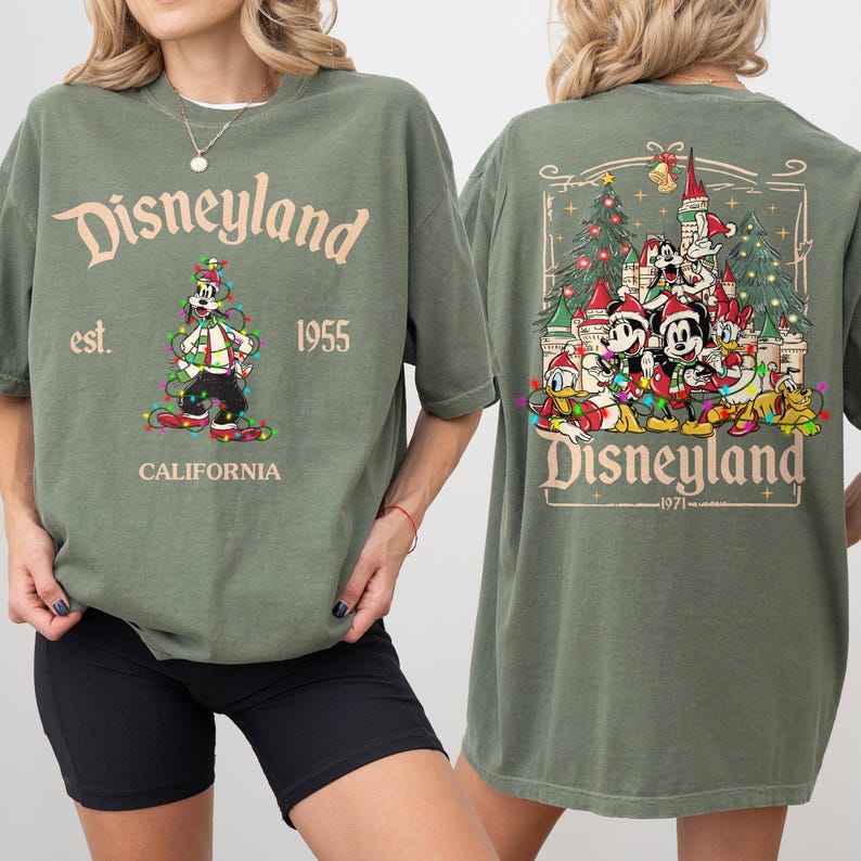 May include: Olive green Disneyland t-shirt. The front features the text "Disneyland est. 1955 CALIFORNIA" with a graphic of Goofy in Christmas lights. The back has a Disneyland graphic with Mickey, Minnie, Donald, and Goofy in Santa hats.