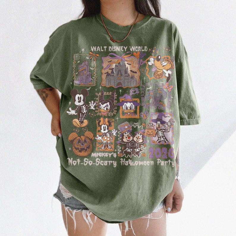 May include: Olive green t-shirt featuring a graphic design for Mickey's Not-So-Scary Halloween Party at Walt Disney World. The design includes cartoon characters, a castle, and the text "2020".