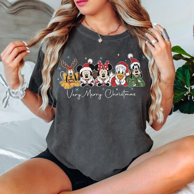Peut inclure: T-shirt gris fonc&eacute; avec un motif de No&euml;l repr&eacute;sentant les personnages Disney Pluto, Mickey Mouse, Minnie Mouse, Donald Duck et Dingo, tous v&ecirc;tus de tenues de f&ecirc;te. L'inscription "Very Merry Christmas" est en dessous.