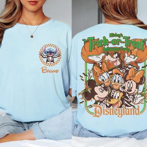 May include: A light blue t-shirt featuring a small circular graphic on the front with a character in a skeleton costume and the name Bruno. The back displays a large graphic of various cartoon characters in skeleton costumes with the text Mickey's Trick-or-Treat Halloween Party Disneyland.