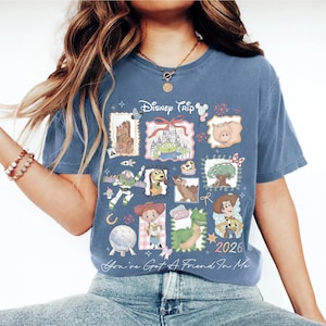 May include: Blue t-shirt featuring a collage of Disney characters and icons. The design includes the text "Disney Trip" and "2026", along with the phrase "You've Got A Friend In Me". The shirt has a vintage, slightly faded look.