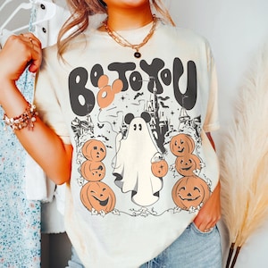 May include: Cream-coloured t-shirt with a Halloween graphic. The design features the text "Boo To You" in black and orange, a ghost, pumpkins, and a castle silhouette. The shirt has a relaxed fit.