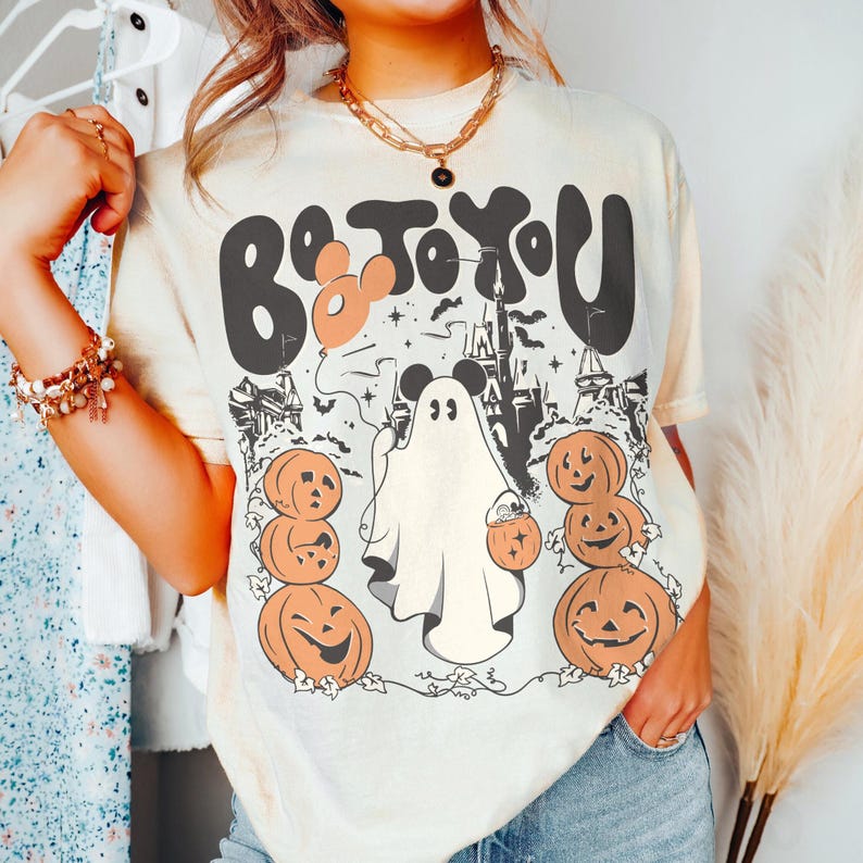 May include: Cream-coloured t-shirt with a Halloween graphic. The design features the text "Boo To You" in black and orange, a ghost, pumpkins, and a castle silhouette. The shirt has a relaxed fit.