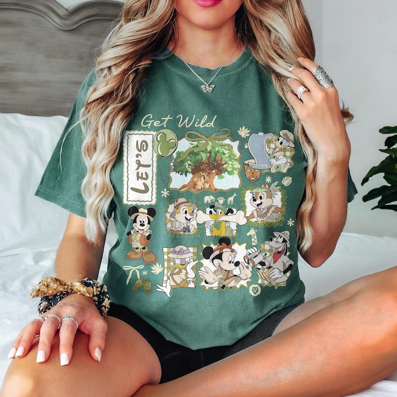 May include: Green t-shirt with a graphic featuring cartoon characters and the text "Get Wild" and "Let's". The design includes images of Mickey Mouse, Donald Duck, Chip and Dale, and other characters in a safari theme.