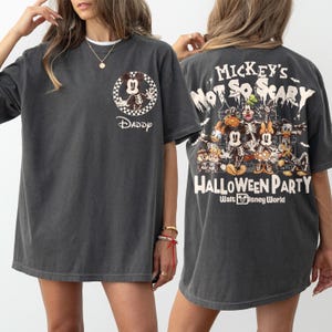 May include: Dark gray t-shirt featuring a skeleton Mickey Mouse design inside a checkered circle, with the word "Daddy" below. The back of the shirt displays "Mickey's Not So Scary Halloween Party" with Disney characters.