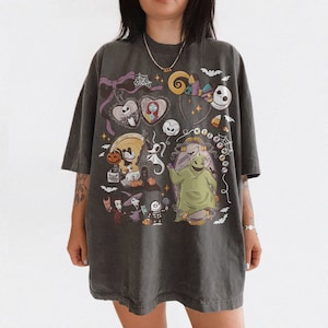 May include: Dark grey t-shirt with a colourful graphic of characters from "The Nightmare Before Christmas." The design includes Jack Skellington, Sally, Oogie Boogie, and other Halloween-themed imagery. The shirt has a relaxed fit.