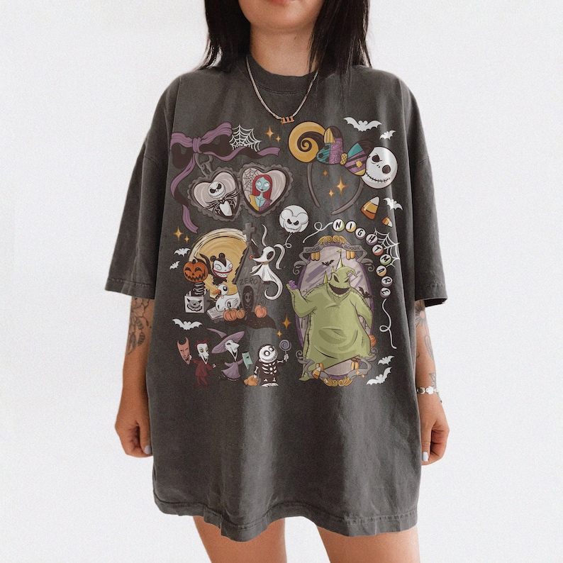May include: Dark grey t-shirt with a colourful graphic of characters from "The Nightmare Before Christmas." The design includes Jack Skellington, Sally, Oogie Boogie, and other Halloween-themed imagery. The shirt has a relaxed fit.