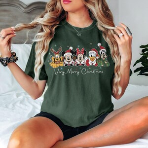Peut inclure: T-shirt vert fonc&eacute; avec des personnages Disney en tenue de No&euml;l. Pluto, Mickey, Minnie, Donald Duck et Dingo sont repr&eacute;sent&eacute;s avec des accessoires festifs. Le texte "Very Merry Christmas" est &eacute;crit en dessous.