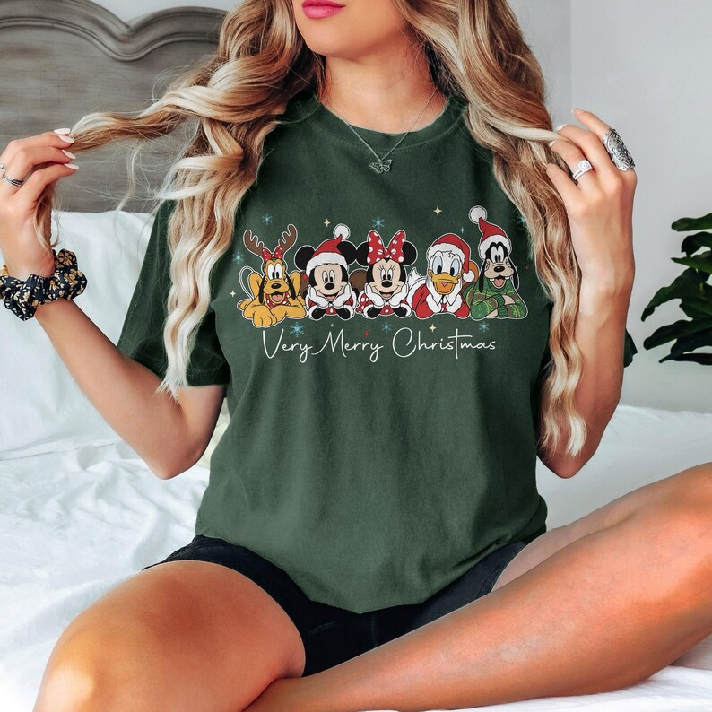 Peut inclure: T-shirt vert fonc&eacute; avec des personnages Disney en tenue de No&euml;l. Pluto, Mickey, Minnie, Donald Duck et Dingo sont repr&eacute;sent&eacute;s avec des accessoires festifs. Le texte "Very Merry Christmas" est &eacute;crit en dessous.