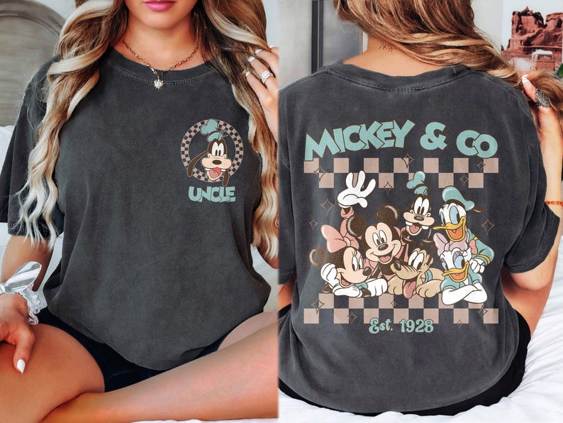 K&ouml;nnte beinhalten: Dunkelgraues T-Shirt mit einem Goofy-Motiv und dem Wort "UNCLE". Auf der R&uuml;ckseite des Shirts sind Micky Maus, Minnie Maus, Donald Duck, Daisy Duck und Goofy mit "MICKEY & CO" und "Est. 1928" abgebildet. Das Design hat einen Retro-Look.