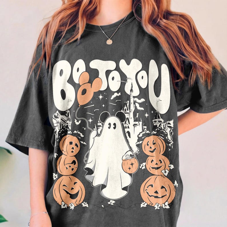 May include: Dark grey t-shirt with a Halloween graphic. The design includes the text "Be to You", a ghost holding a pumpkin bucket, pumpkins, and a castle silhouette. A balloon is also included in the design.