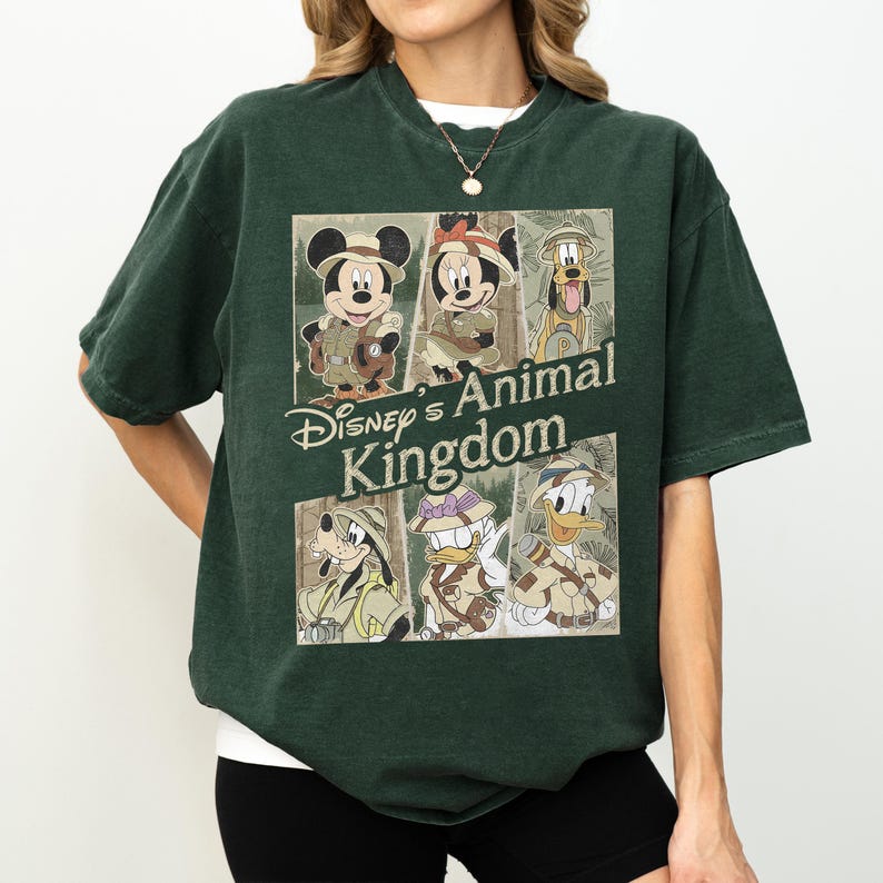 May include: Dark green t-shirt featuring a graphic of Disney characters in safari outfits. The graphic includes Mickey Mouse, Minnie Mouse, Goofy, Donald Duck, and more, with the text "Disney's Animal Kingdom".