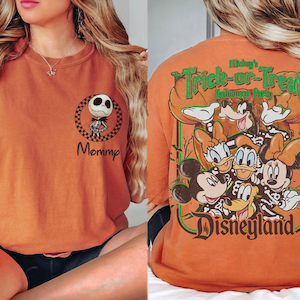 May include: An orange t-shirt featuring a small graphic on the front left chest of Jack Skellington inside a checkered circle with the word Mommy below it. The back displays a large graphic of Disney characters in skeleton costumes.