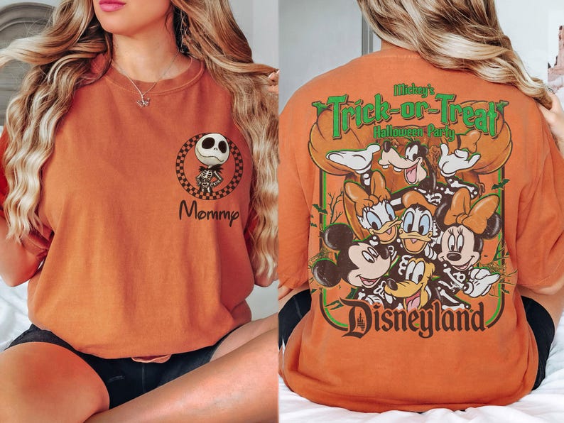 May include: An orange t-shirt featuring a small graphic on the front left chest of Jack Skellington inside a checkered circle with the word Mommy below it. The back displays a large graphic of Disney characters in skeleton costumes.