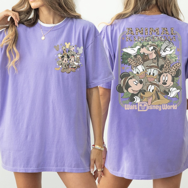 Puede incluir: Una camiseta de color lila con gr&aacute;ficos de personajes de Disney en la parte delantera y trasera. El gr&aacute;fico frontal incluye a Mickey Mouse, el Pato Donald y Goofy. El gr&aacute;fico trasero dice "Animal Kingdom" y "Walt Disney World".