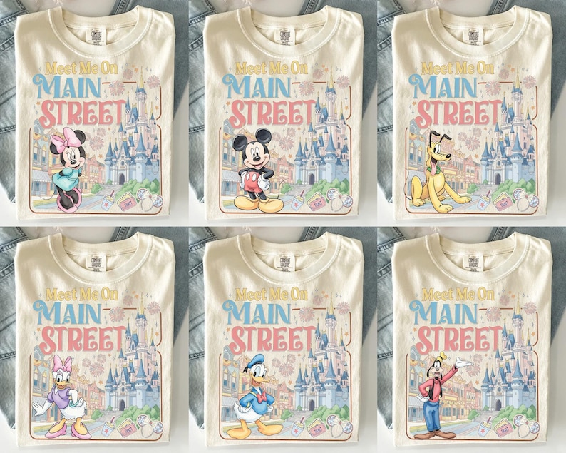 K&ouml;nnte beinhalten: Cremefarbene T-Shirts mit dem Text "Meet Me On Main Street" und verschiedenen Zeichentrickfiguren. Die Shirts zeigen Minnie Mouse, Mickey Mouse, Pluto, Daisy Duck, Donald Duck und Goofy, mit einer Schlosskulisse.