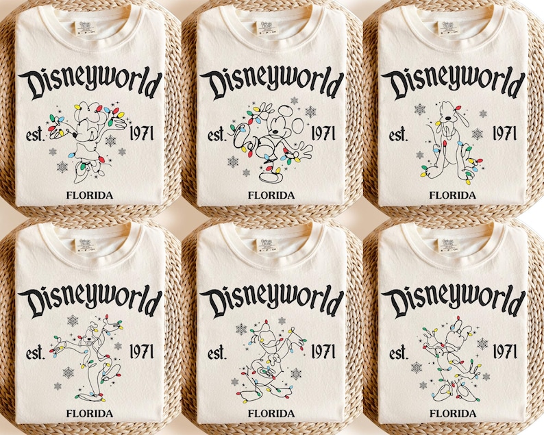 May include: Cream-coloured t-shirts with the text "Disneyworld" above the text "est. 1971 FLORIDA". Each shirt features a different cartoon character decorated with Christmas lights. The shirts are folded and arranged on a woven surface.