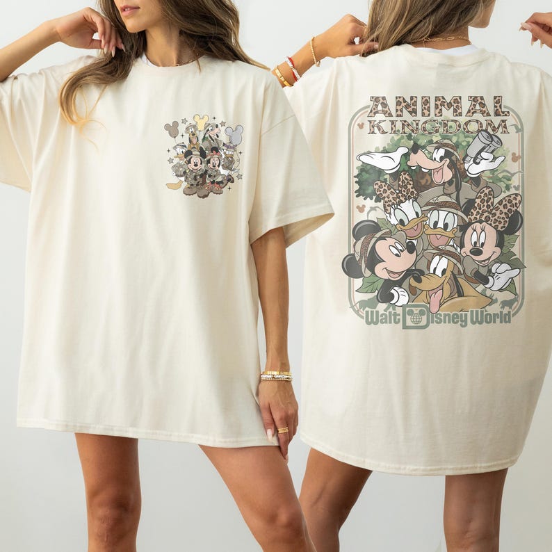 Puede incluir: Camiseta color crema con un gr&aacute;fico de personajes de Disney. La parte delantera tiene un peque&ntilde;o dise&ntilde;o de Mickey Mouse, Minnie Mouse y amigos. La parte trasera muestra un dise&ntilde;o m&aacute;s grande con las palabras "ANIMAL KINGDOM" y "Walt Disney World".
