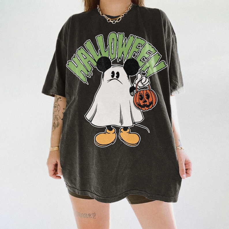 May include: Dark gray t-shirt with a Halloween-themed graphic. The design features a cartoon ghost with Mickey Mouse ears holding a jack-o'-lantern. The word "HALLOWEEN" is printed above the character in green letters.