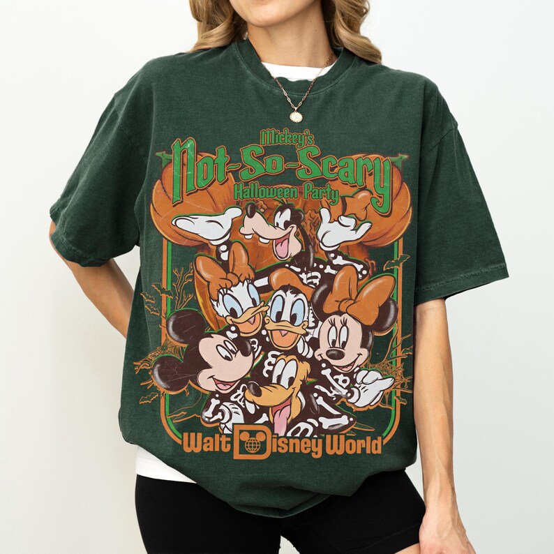 May include: A dark green short-sleeve t-shirt featuring a graphic print of Disney characters in skeleton costumes. The text reads Mickey's Not-So-Scary Halloween Party and Walt Disney World. The design includes pumpkins and bats in orange and green.