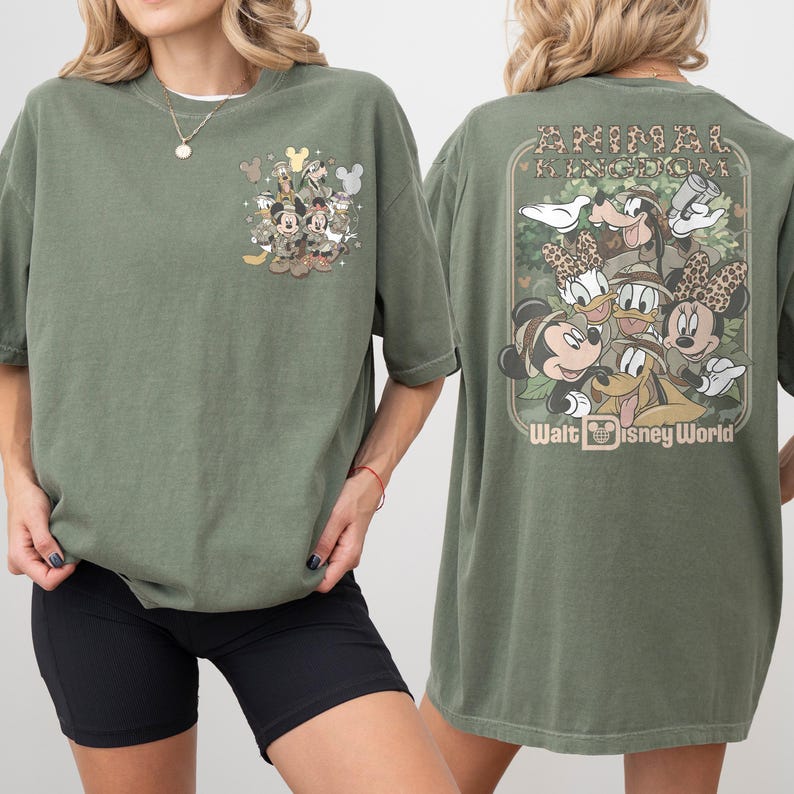 Puede incluir: Camiseta verde oliva con un gr&aacute;fico de personajes de Disney. La parte delantera tiene un dise&ntilde;o peque&ntilde;o, mientras que la parte trasera muestra una imagen m&aacute;s grande con el texto "ANIMAL KINGDOM" y "Walt Disney World".