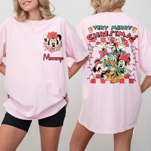 May include: Pink t-shirt featuring Minnie Mouse with a red bow and the word "Mommy". The back of the shirt displays a "Very Merry Christmas" design with Disney characters. The shirt has short sleeves.